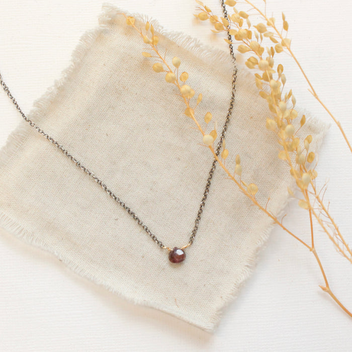 The little garnet drop mixed metal necklace styled on tan linen with dried grass