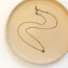 The little garnet drop necklace styled on a tan plate to show the adjustable lobster clasp closure