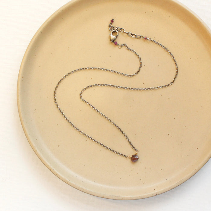 The little garnet drop necklace styled on a tan plate to show the adjustable lobster clasp closure