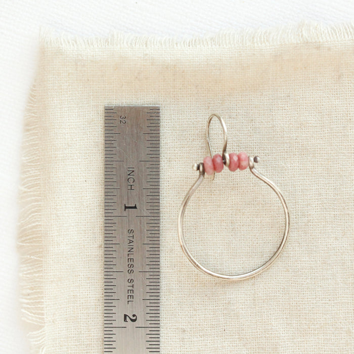 A rhodonite halo hoop earring next to a ruler for size reference