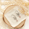 The rhodonite sprout earrings styled on wood with linen, dried grass, and a lace doily 
