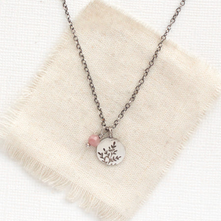 The rhodonite and sprout charm necklace styled on tan linen