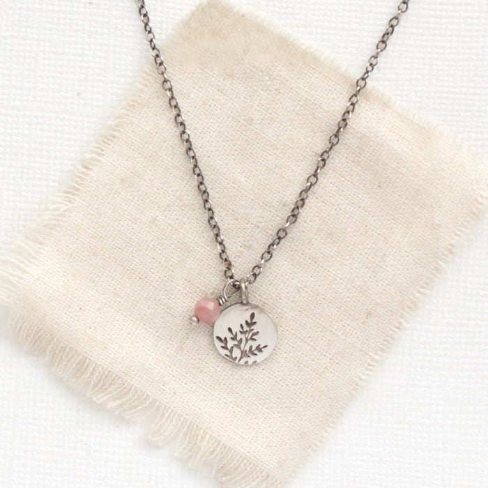 The rhodonite and sprout charm necklace styled on tan linen