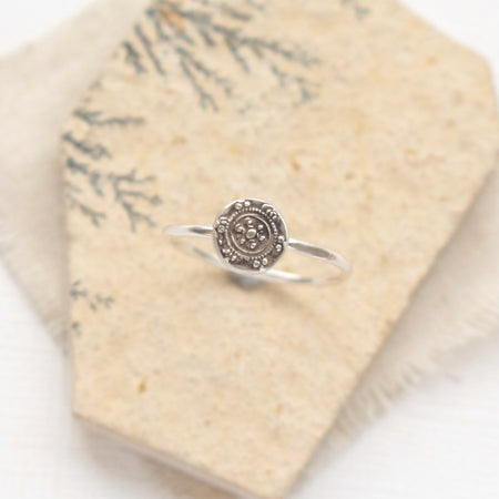 The roma embossed silver stacking ring styled on a tan rock with tan linen