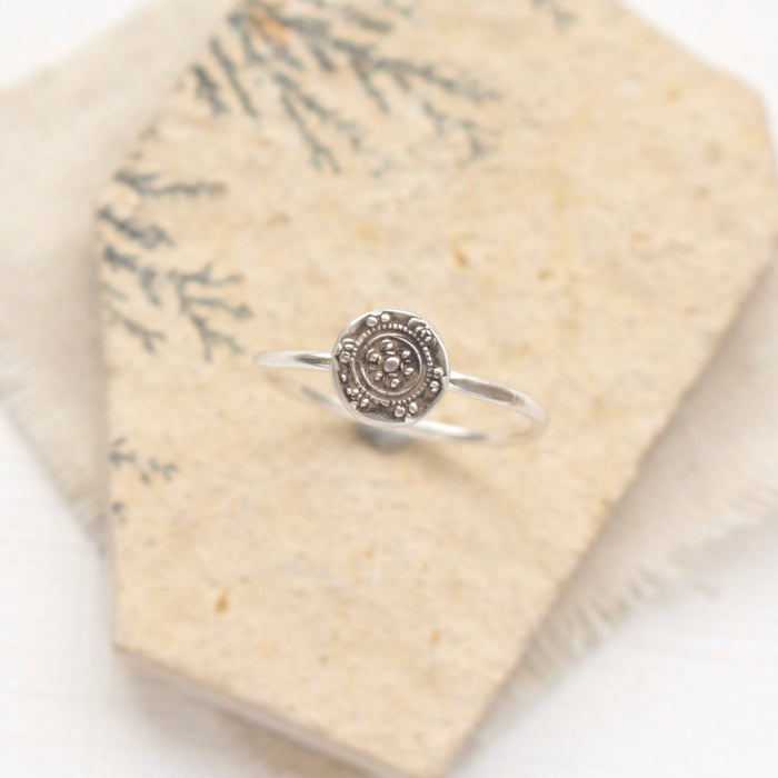 The roma embossed silver stacking ring styled on a tan rock with tan linen