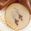 The mini cactus flower violet dangle earrings styled on wood with orange velvet and dried grass