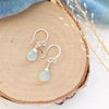 The silver chalcedony drop earrings styled on wood with blue velvet and dried grass