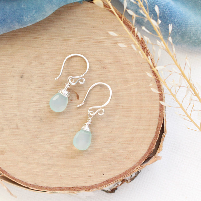 The silver chalcedony drop earrings styled on wood with blue velvet and dried grass