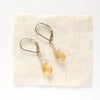 The silver citrine drop earrings styled on tan linen