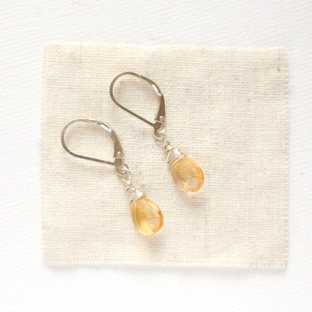 The silver citrine drop earrings styled on tan linen
