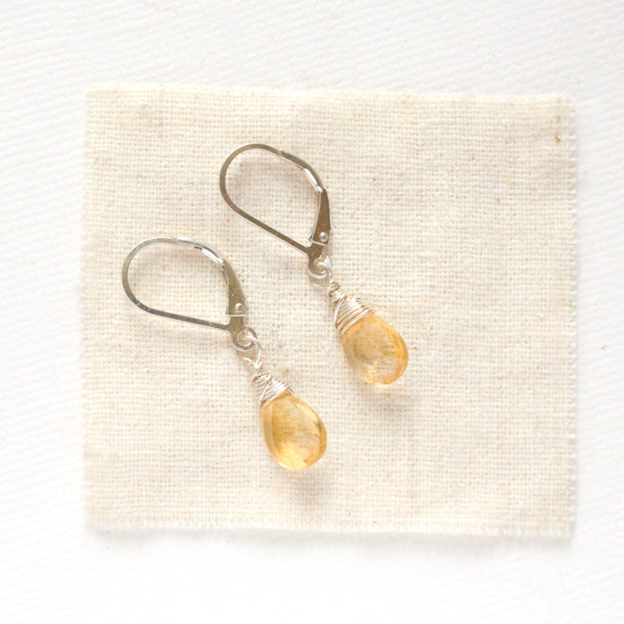 The silver citrine drop earrings styled on tan linen