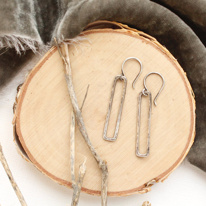 The silver open bar earrings styled on wood with gray velvet and dried grass