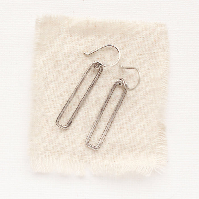 The silver open bar earrings styled on tan linen