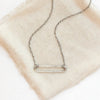 The silver open bar necklace styled on tan linen