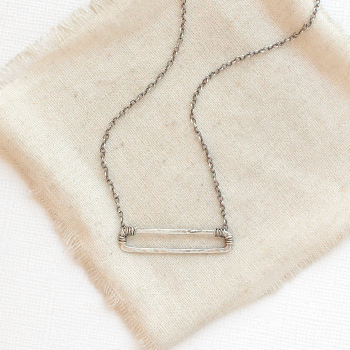 The silver open bar necklace styled on tan linen