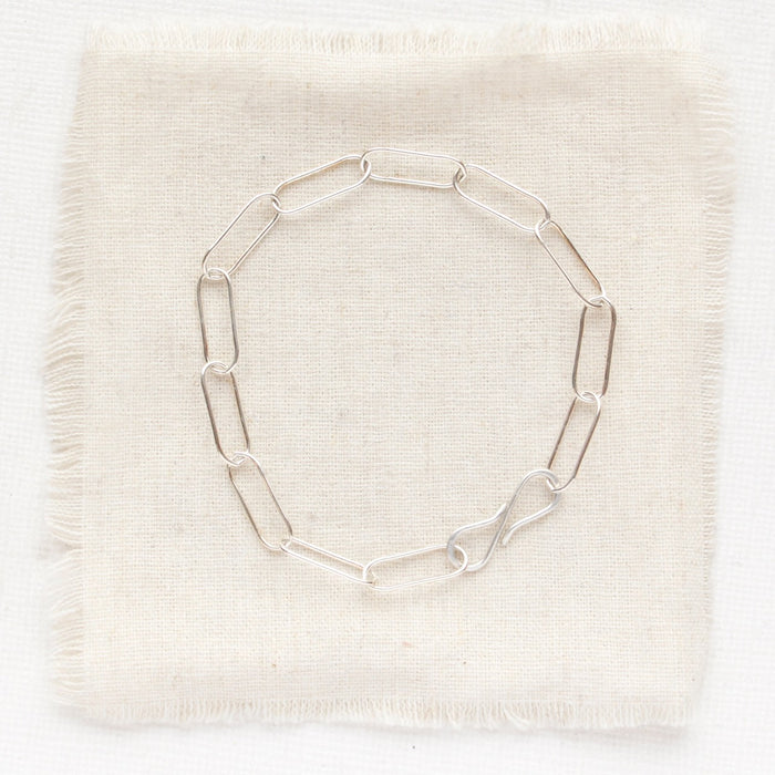 The silver paperclip bracelet styled on tan linen