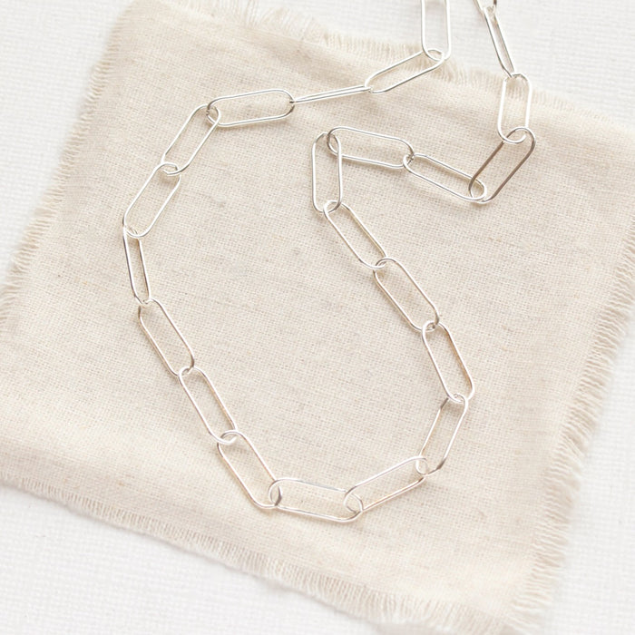 The bright silver paperclip necklace styled on tan linen