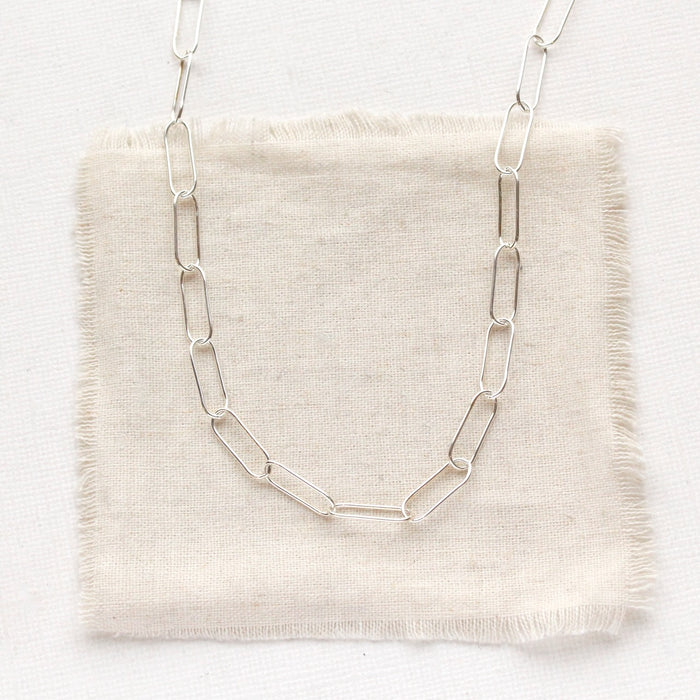 The bright silver paperclip necklace styled on tan linen