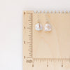The pinned silver pearl earrings styled on a wooden ruler for size reference