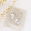 The silver pinned pearl earrings styled on tan linen with dried grass