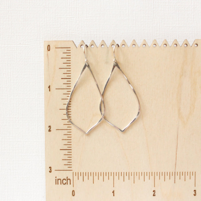 The silver pointed hoop earrings on a wooden ruler for size reference