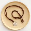 The silver wanderer medallion adjustable leather necklace styled on a tan plate to show the whole necklace 