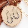 The speckled turquoise columbine hoop earrings styled on wood with orange velvet and dried grass