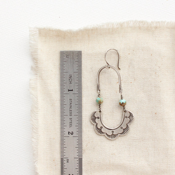 A speckled turquoise columbine hoop earring next to a ruler for size reference
