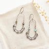 The speckled turquoise columbine hoop earrings styled on tan linen with dried grass