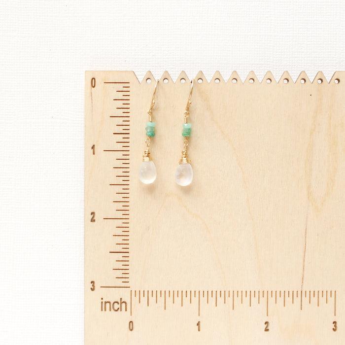 The stacked emerald and moonstone drop earrings on a wooden ruler for size reference