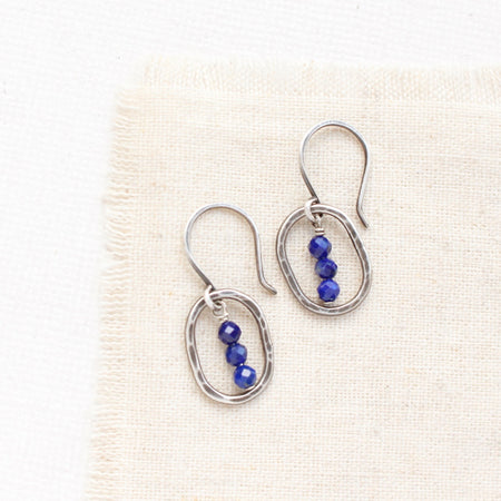 The stacked lapis mini hoop earrings styled on tan linen