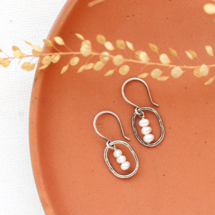 The stacked pearl mini hoop earrings styled on an orange plate with dried grass