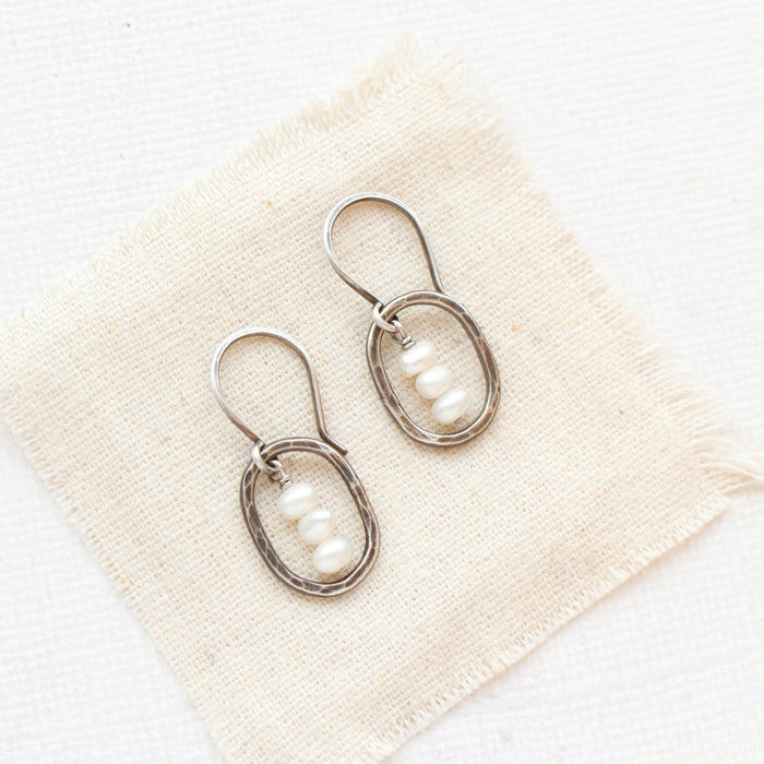 The stacked pearl mini hoop earrings styled on tan linen