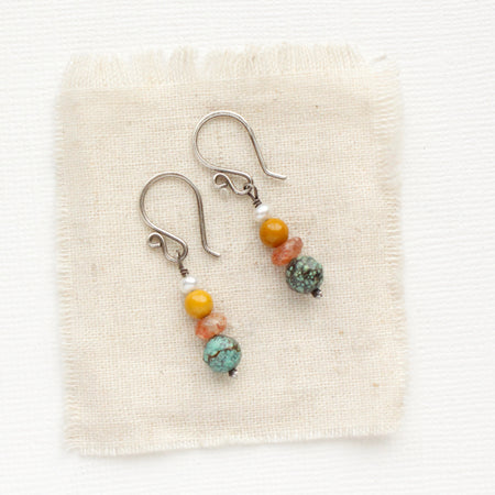 The stacked sunset earrings styled on tan linen