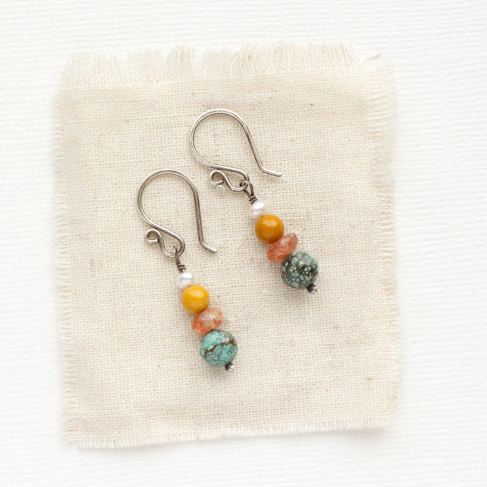 The stacked sunset earrings styled on tan linen