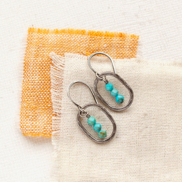 The stacked turquoise mini hoop earrings styled on tan and orange linen