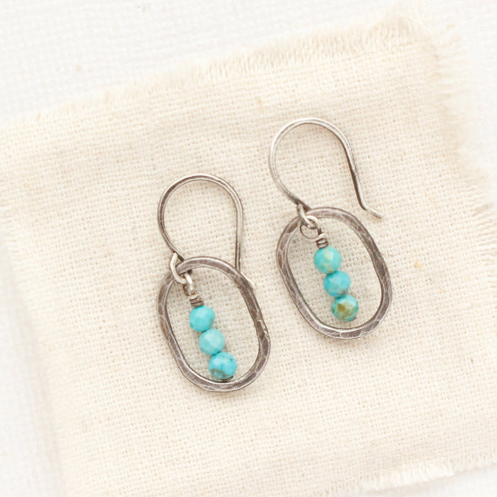 The stacked turquoise mini hoop earrings styled on tan linen
