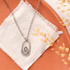 The wanderer hoop necklace styled on an orange plate with linen and dried grass
