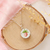 The strawberry bud vintage plate necklace styled on wood with pink velvet and dried grass