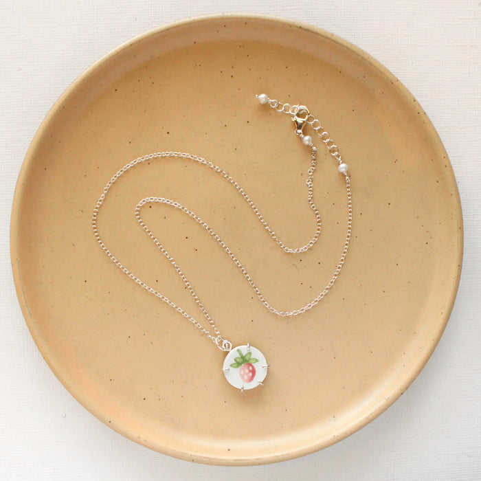 The strawberry bud vintage plate necklace styled on a tan plate to show the adjustable lobster clasp closure