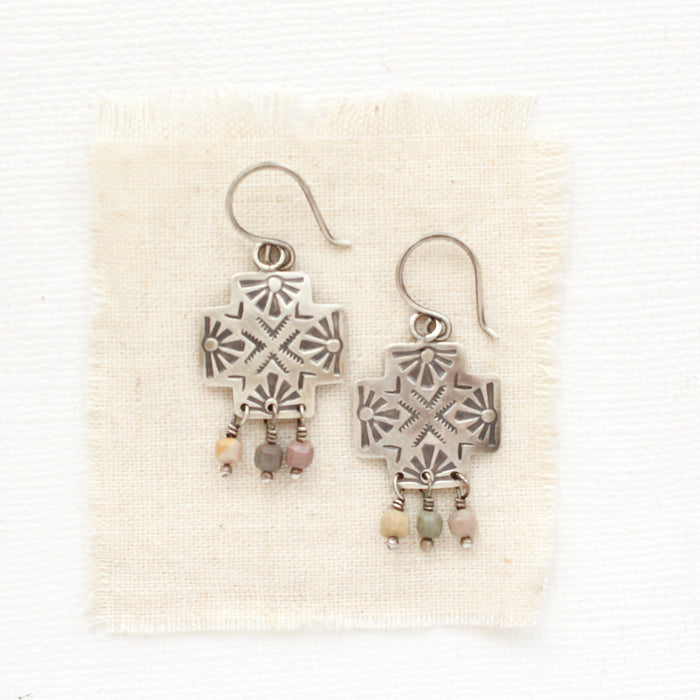 The sun cross rainbow agate earrings styled on tan linen