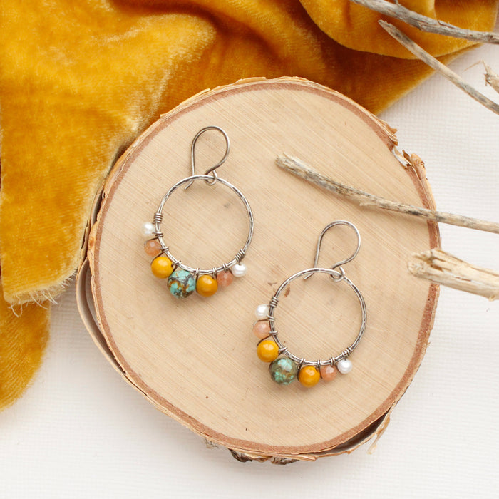 The sunset hoop earrings styled on wood with yellow velvet and dried grass