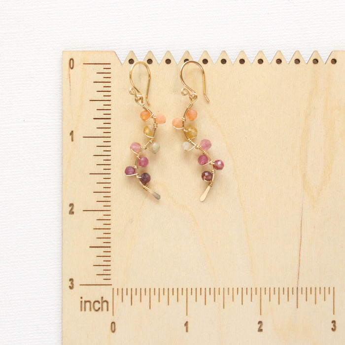 The sunset vine earrings on a wooden ruler for size reference