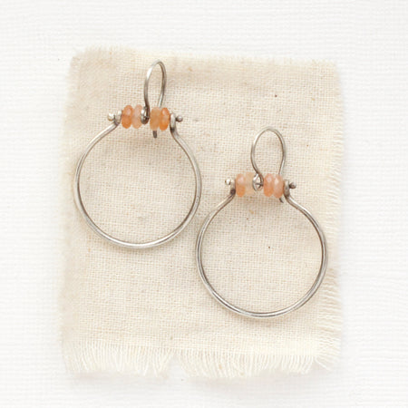 The sunstone halo hoop earrings styled on tan linen