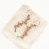 The sunstone wrapped silver vine earrings styled on tan linen