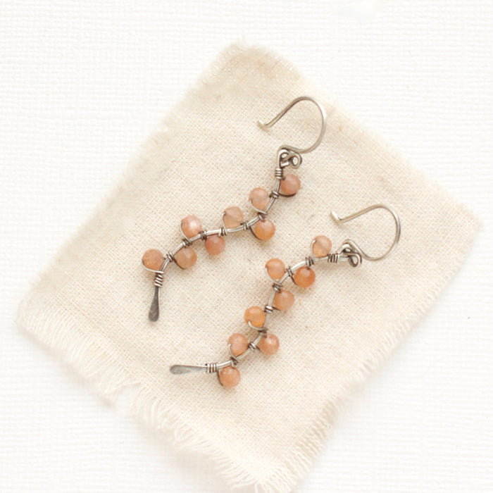 The sunstone wrapped silver vine earrings styled on tan linen