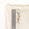 A sunstone wrapped silver vine earring next to a ruler for size reference