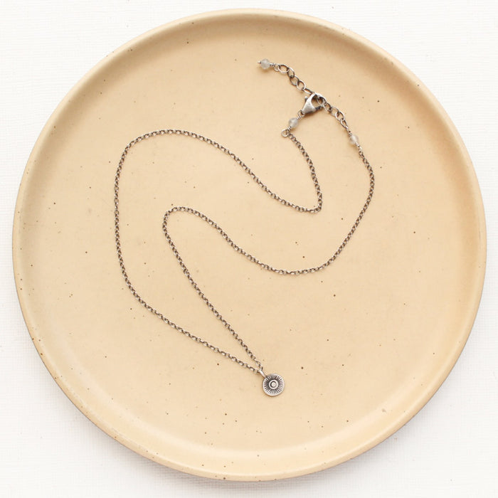 The mini talara sun necklace styled on a tan plate to show the adjustable clasp closure