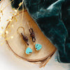 The turquoise and leather earrings styled on wood with blue velvet and dried grass