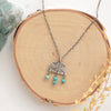 The turquoise fringe pakal arch necklace styled on wood with a green rock and dried grass